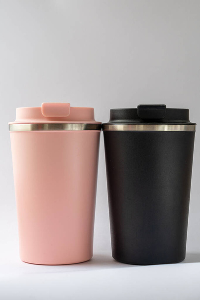 Zwei Thermoskannen oder Thermoskannen für Tee oder Kaffee vor weißem Hintergrund. Schwarz und rosa für sie und ihn. Heißgetränk für Paare - Foto, Bild