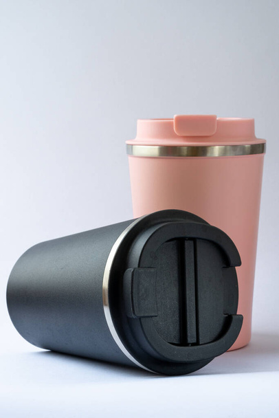 Two thermo cups or thermos mugs for tea or coffee against a white background. Black and pink for him and her. Hot beverage for couples - Foto, imagen