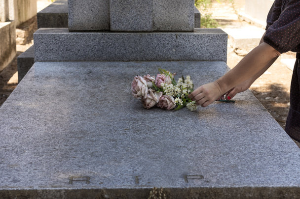 Dłonie kobiety kładą bukiet kwiatów na marmurowym grobowcu na cmentarzu. Jest to szary marmurowy grobowiec z inicjałami RIP po łacinie i nieostrym tłem.. - Zdjęcie, obraz