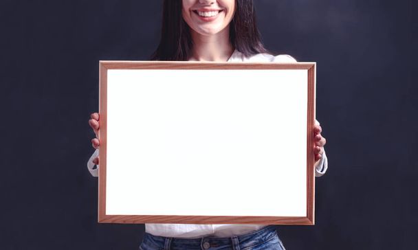 Smiling woman holding blank billboard. Girl in white shirt with poster frame - Фото, зображення