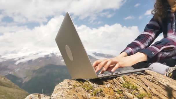 Руки женщины крупным планом работают за ноутбуком на большом камне на фоне гор, женщина-фрилансер работает на открытом воздухе в палатке - Кадры, видео