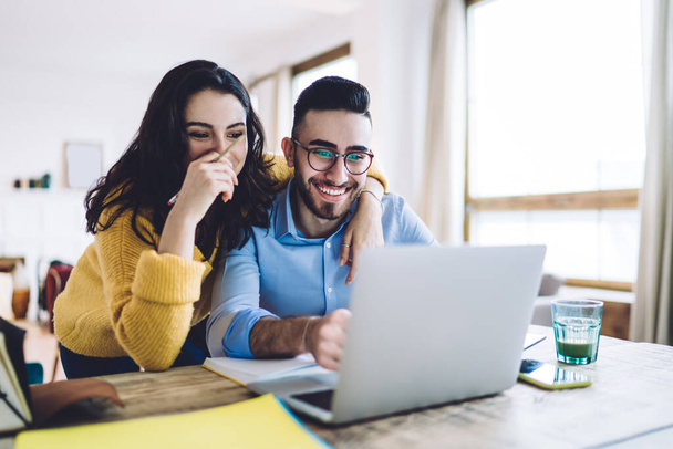 Cheerful man and woman with pencil in had near face smiling while planning further work together and using laptop at home  - Φωτογραφία, εικόνα