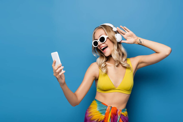 onnellinen nainen langattomissa kuulokkeissa ja bikinit top holding älypuhelin sininen - Valokuva, kuva