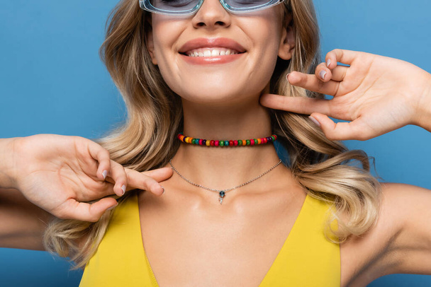 cropped view of joyful young woman in beaded colorful necklace smiling isolated on blue - Foto, immagini