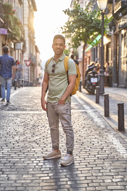 Jeune Latino souriant marchant dans les rues de la ville. Homme latin en jeans et polo vert.  - Photo, image
