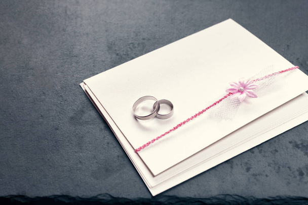 ピンクの花で飾られた封筒と黒の背景に2つの結婚指輪 - 写真・画像