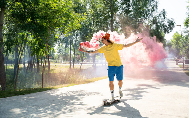 Skaters with colored smoke bombs. Professional skateboarders having fun at the skate park - Foto, imagen