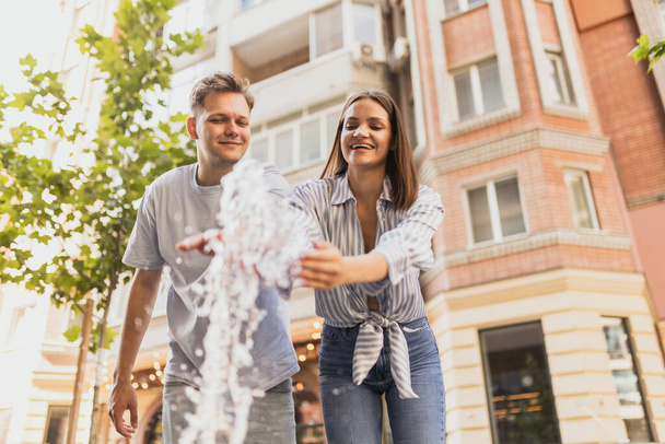 Photo of young couple having fun near fountain outdoors on warm summer day - Photo, Image