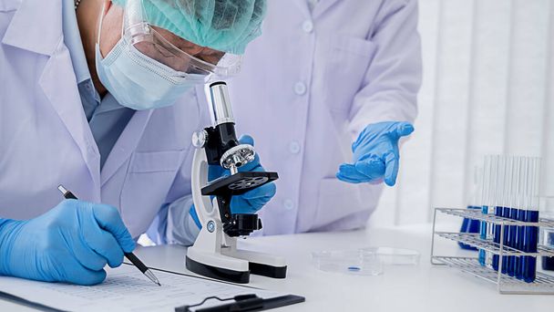 Chercheur médical ou scientifique ou médecin de l'homme regardant une éprouvette de solution claire dans un laboratoire - Photo, image