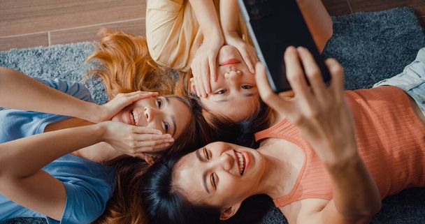 Por encima de la vista de cerca grupo de señoras de Asia con la felicidad disfrutar del momento mantenga el teléfono inteligente sonriendo tomar recuerdos foto tumbado en la alfombra en el piso de la sala de estar en casa. Concepto de cuarentena de la actividad del estilo de vida. - Foto, Imagen