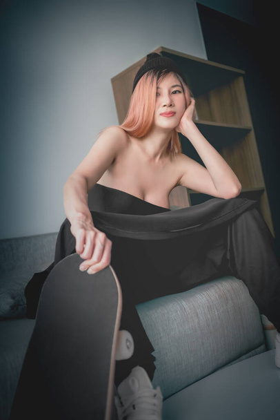 Ázsiai szexi modell lány gördeszka pózol kanapén egy lakás utcai divat. - Fotó, kép