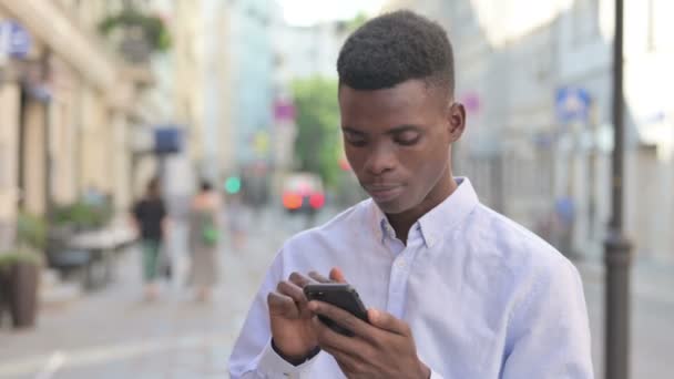 African Man Γιορτάζοντας στο Smartphone, ενώ στέκεται Εξωτερική - Πλάνα, βίντεο