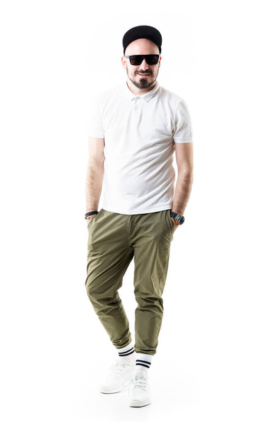 Happy comfortable stylish young man wearing chino pants cap and sunglasses smiling. Full length portrait isolated on white background - Photo, Image