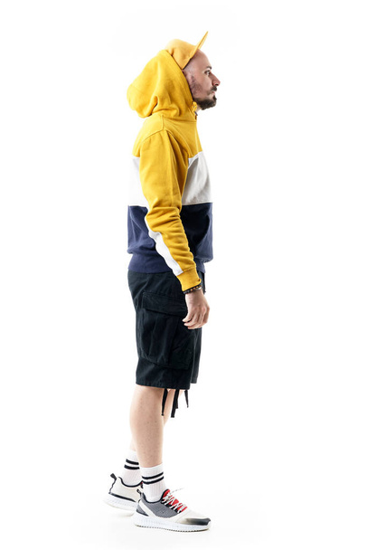 Side view of urban style cool young man with cap in hoodie and capri pants walking. Full length portrait isolated on white background - Photo, image