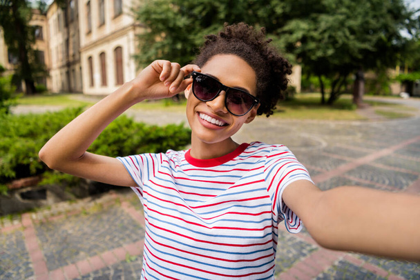 Foto de la joven alegre chica africana feliz sonrisa positiva hacer selfie mano toque sunglass viaje verano al aire libre - Foto, imagen