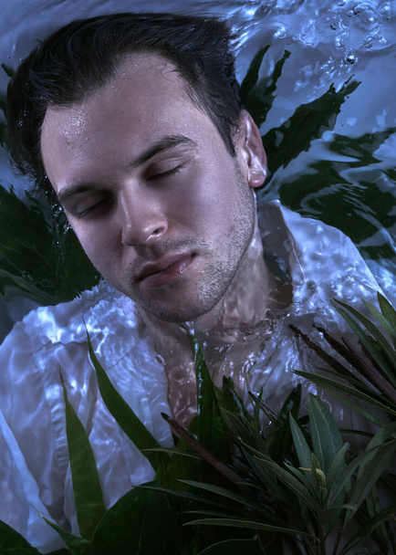 Close-up fashion portrait of caucasian handsome unshaven man underwater in sexy wet white shirt closed eyes strong face, plants background - Fotó, kép