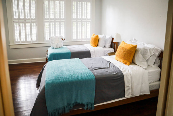 ターコイズとグレーのベッドスプレッドと黄色の装飾枕を備えた2つのツインベッドルーム - 写真・画像