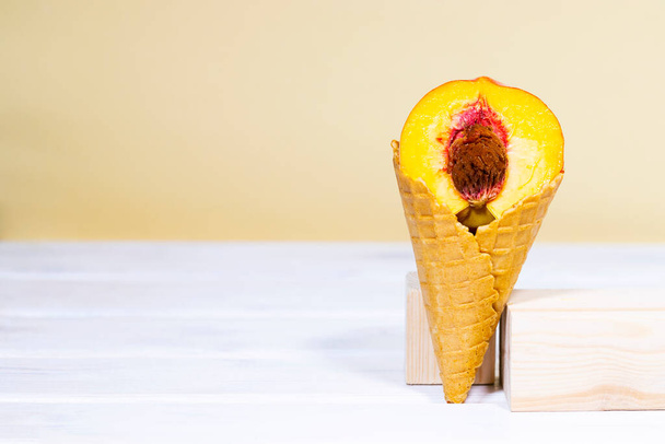 Half a ripe peach in sweet wafer cone on wooden stands over light orange background. Healthy nutrition, seasonal harvest of fruits. Copy space, Equilibrium floating food balance - Photo, image