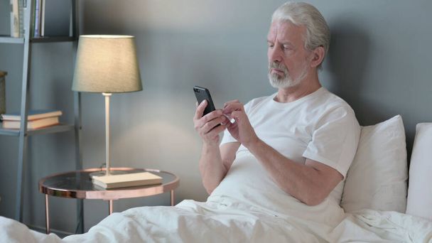 Использование смартфона старшим стариком в постели - Фото, изображение