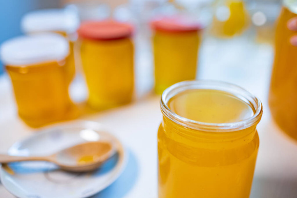 Composition of several jars with honey and a saucer with a wooden spoon on a white table - Foto, Imagem