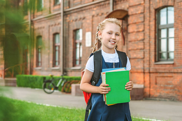 Portrait of a young girl in a school uniform with books in her hands. Against the background of an old college. Back to school concept - Foto, Bild