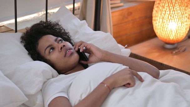 Jeune femme africaine parlant au téléphone posant au lit - Photo, image