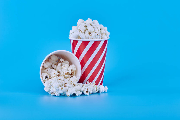 Két piros pohár popcorn kék alapon, Odi tele van popcornnal, a másik pedig morzsás popcornnal. - Fotó, kép