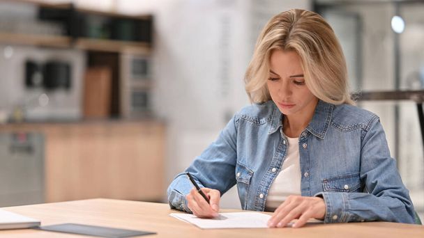 Jonge casual vrouw schrijven op papier op het werk - Foto, afbeelding