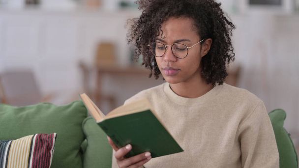 Молода африканка, яка читає книжку вдома - Фото, зображення
