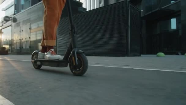 Baja sección de seguimiento de tiro de piernas de hombre irreconocible montar scooter eléctrico en la carretera en la ciudad - Metraje, vídeo