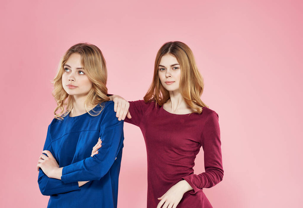 schattig vriendinnen in jurken staan naast vriendschap roze achtergrond - Foto, afbeelding