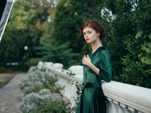 bella donna appoggiata alla ringhiera in un parco verde vestito a piedi - Foto, immagini