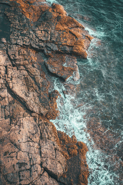 An aerial shot of a rocky seashore and waves crashing into them - Foto, Bild