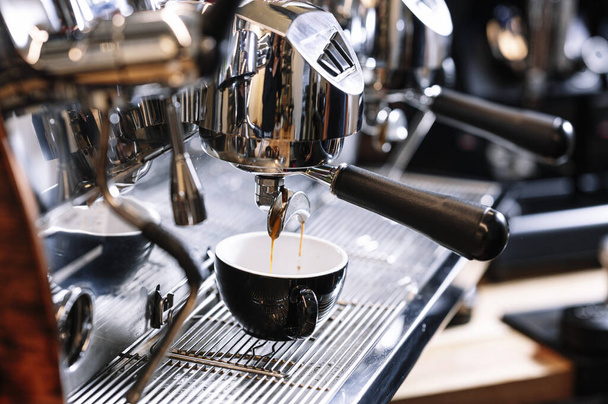 A closeup shot of espresso-making process with coffee cup under portafilter of modern coffee machine - Foto, Imagem