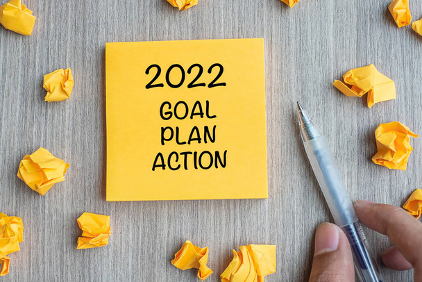 2022 Στόχος, Σχέδιο, Δράση λέξη σε κίτρινο σημείωμα με Businessman κρατώντας στυλό και θρυμματισμένο χαρτί σε ξύλινο φόντο τραπέζι. Νέο Έτος Νέο Έναρξη, Αποφάσεις, Στρατηγική έννοια - Φωτογραφία, εικόνα