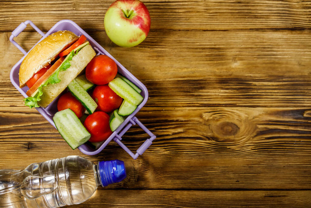 Bottle of water, apple and lunch box with burgers and fresh vegetables on a wooden table. Top view, copy space - Photo, Image