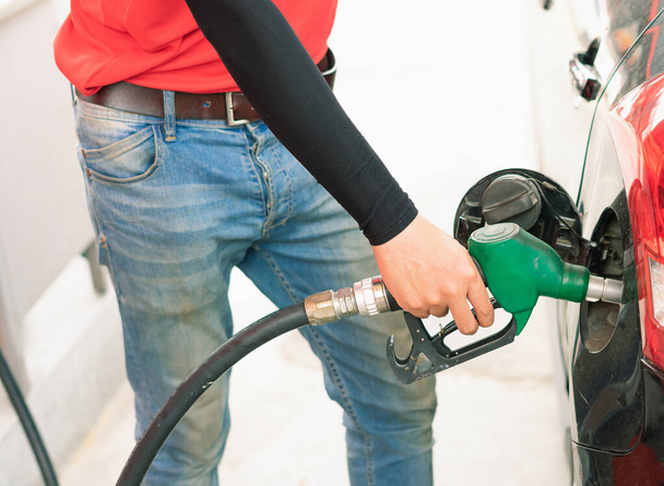 Asian gas station worker man catching green fuel nozzle into one hand while filling high energy power fuel into black auto car tank in petrol station, commercial service for benzine, diesel, gasohol, gasoline. - Foto, imagen
