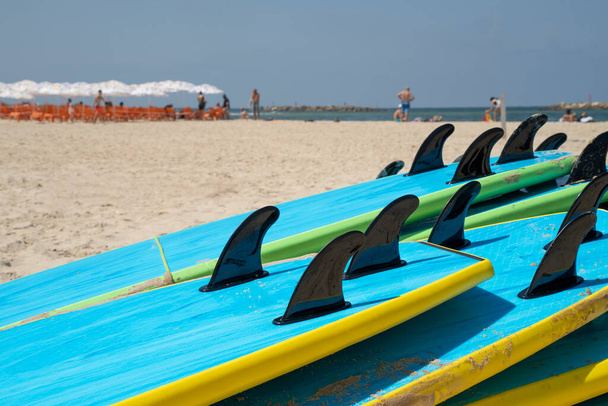 Una pila di tavole da surf su una spiaggia di sabbia a Tel Aviv, Israele, in una giornata di sole. Bagnanti sullo sfondo. - Foto, immagini