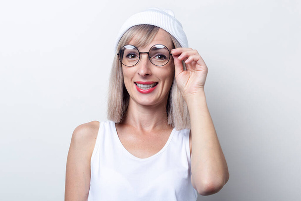 Usmívající se mladá žena v bílém klobouku a brýle na světlém pozadí. - Fotografie, Obrázek