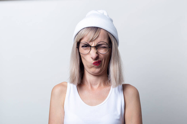 Young woman squinting grimace glasses, a white cap on a light background. - Photo, Image