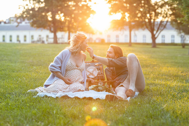 Красива вагітна пара має пікнік на заході сонця надворі
 - Фото, зображення