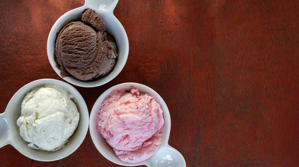 Copas de diferentes sabores de helado, vainilla, chocolate y fresa en pequeñas tazas de cerámica blanca. - Foto, imagen