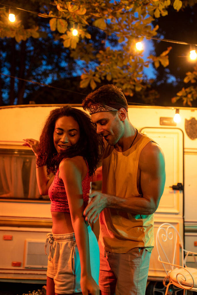 Young couple on vacation with the camper. Dancing outdoor in the night. Concept about wanderlust road trips and lifestyle on vacation - Photo, Image