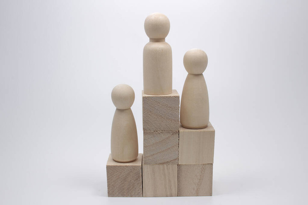 Tres figuras de madera de los hombres en cubos de juguete se encuentran en orden jerárquico como lugares de premio - Foto, Imagen