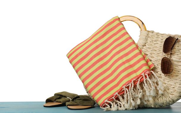Beach bag with towel, slippers and sunglasses on light blue wooden surface against white background - Photo, Image