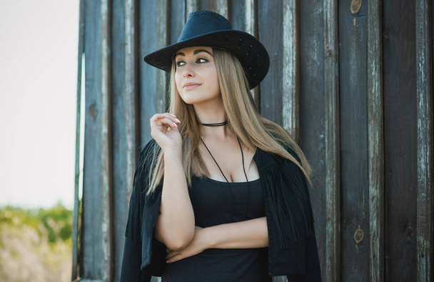 Girl in American country style black boho jacket with a fringe and cowboy hat at nature - Φωτογραφία, εικόνα