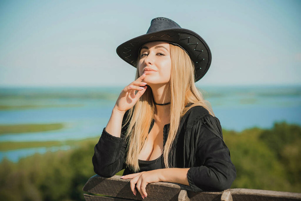 Girl in American country style black boho jacket with a fringe and cowboy hat at nature - Photo, Image