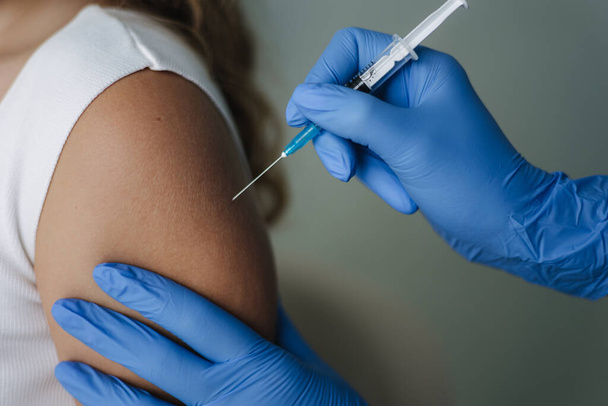 Kobieta-lekarz w rękawiczkach ochronnych trzymająca strzykawkę wykonującą szczepionkę przeciw wirusowi Covid 19. Kobiety dostają zastrzyk w ramię. Koncepcja badań klinicznych szczepionki, wirus korony - Zdjęcie, obraz