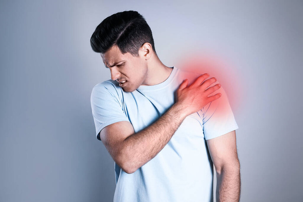 Mann mit Schulterschmerzen vor grauem Hintergrund - Foto, Bild