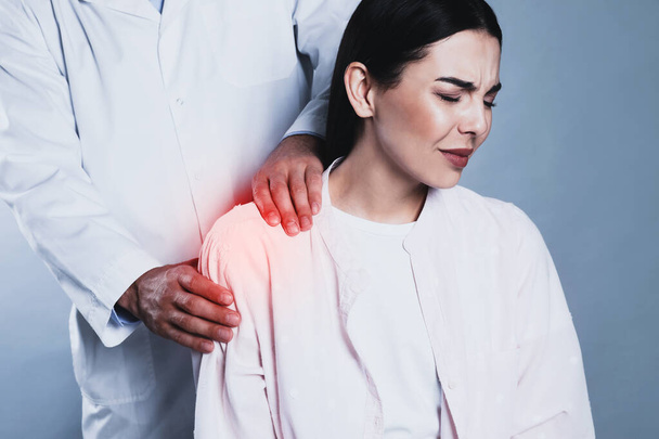 Doctor examining woman with shoulder pain on grey background - Foto, Bild